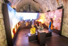 Wenn der Boden bebt: Neues immersives Erlebnis auf der Festung Königstein

Ein neues LED-Wall-Panorama mit Kinosound und Bodenvibration nimmt Besucher der Festung Königstein mitten hinein in den Verteidigungsfall. Es ist eines der intensivsten Festungserlebnisse in Deutschland. Am Freitag startet es.

Königstein/Sächs. Schweiz, 28. Mai 2026 (tpr) – Erst ein Grollen. Dann bebt der Boden. Kanonenschüsse dröhnen zwischen den hohen Mauern, eine Armee rückt näher – in ihr sicheres Verderben. Zum Glück ist alles nur Simulation, wenn auch eine wissenschaftlich fundierte und technisch sehr aufwendig präsentierte. Mit einer neuen Installation aus 180-Grad-LED-Wall-Panorama, Kinosound und Bodenvibration demonstriert das Museum Festung Königstein erstmals das ausgeklügelte und praktisch unüberwindliche Verteidigungssystem der historischen Wehranlage in Aktion. Am Freitag wird die neue Station in Betrieb genommen.

„Wir bieten ein mitreißendes Eintauchen in die Logik dieser Festung. Für drei Minuten erwachen Kanonen, Tore, Brücken und Sperren zum Leben. Man versteht nicht nur, warum der Königstein als uneinnehmbar galt – man fühlt es“, sagt André Thieme, Geschäftsführer der Festung Königstein.

Für das Museum ist es ein bedeutender Schritt auf dem Weg von der Information zur Immersion. Geschichte als multimediales Erlebnis, das den Besucher mitten hinein nimmt ins Geschehen: Das ist Trend in der deutschen Museumslandschaft. Eine Besonderheit der neuen Installation auf dem Königstein ist, dass die Inszenierung inmitten der historischen Verteidigungsarchitektur zu erleben ist. Authentischer Schauplatz, wissenschaftlich fundierte Rekonstruktion und moderne Erlebnisdramaturgie verschmelzen zu einem Erlebnis, das bundesweit beispielhaft zeigt, wie komplexe Festungsgeschichte emotional, verständlich und physisch erfahrbar vermittelt werden kann.

Kein Feldherr wagte je einen Angriff

Die Festung Königstein zählt zu den bedeutendsten Bergfestungen Europas. Hoch über der Elbe, über steilen Sandsteinwänden und hinter massiven Mauern auf einem Tafelberg gelegen und ausgestattet mit einem mächtigen Verteidigungssystem galt die Festung als Sinnbild sächsischer Wehrhaftigkeit. Ihre abschreckende Stärke schützte sie zuverlässig vor Eroberungsversuchen.

Genau darin lag die Herausforderung der Produktion. Verantwortet wurde sie von dem vielfach prämierten deutschen Studio für digitale Erlebniswelten Faber Courtial, das unter anderem die erste vollimmersive VR-Dokumentation für das deutsche Fernsehen produzierte. Die gestalterische Umsetzung des Ausstellungsbereichs koordinierte Whitebox aus Dresden. Ursprünglich entstand der Film für eine Sonderausstellung der Festung Königstein in China im Jahr 2025 – mit dem Ziel, ihn anschließend auch am Originalschauplatz auf dem Königstein zu präsentieren. Für die Installation auf der Festung wurde die Inszenierung noch einmal weiterentwickelt.

Ein System aus Feuer, Fallen und Felsen

Der Film zeigt die Wucht und Präzision des Verteidigungssystems der Festung Königstein. Die Besucher erleben, wie Hindernisse, Feuerlinien, Fallvorrichtungen und Gelände ineinandergriffen und den einst einzigen Aufgang zum etwa 40 Meter höher gelegenen Festungsplateau zu einer nahezu unüberwindbaren Abfolge von Gefahren machten.

Zu sehen sind die Kanonenstellungen der Festung, die Wippbrücke, gestaffelte Verteidigungspositionen, Tore, Barrikaden, der mit Eisenstacheln versehene Spanische Reiter, Kartätschenfeuer aus der Grabenschere sowie Steinschmeiße, Pechnase und Fallpalisade in der Dunklen Appareille. „Die Anlagen wurden vom 16. bis 19. Jahrhundert errichtet und sind bis heute erhalten. Entlang des Aufgangs zur Festung können Besucher sie entdecken“, erklärt Markus Bitterlich, Abteilungsleiter Museum der Festung Königstein. „Im Film sind sie nun erstmals auch in Aktion erfahrbar.“

Die Inszenierung ist ab Freitag dauerhaft und in fünf Sprachen sowie mit Untertitel erlebbar. Sie ist im Festungseintritt inbegriffen. Um sie zu Beginn des Festungsbesuchs zu sehen, sollte der fußläufige Aufstieg – nicht der Felsenlift – gewählt werden. Empfohlen wird der Film ab einem Alter von acht Jahren. 

Foto: Marko Förster
28.05.2026 © Marko Förster